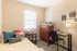 Bright and cozy bedroom with stylish decor, featuring a comfortable bed, a sleek desk, and natural light streaming in through a window.