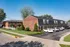 Charming brick apartment complex with spacious parking, surrounded by lush greenery and a clear blue sky.