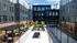 Modern apartment courtyard featuring sleek black and brick facades, lush greenery, comfortable seating areas, and a ping-pong table under a clear blue sky.