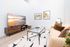 Modern living room with a cozy beige sofa, stylish glass coffee table, and large TV displaying a serene beach scene. Bright, minimalist decor with wooden accents enhances a welcoming ambiance.
