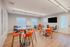 Modern community room featuring vibrant orange seating, sleek tables, a large flat-screen TV, and elegant wood flooring, perfect for gatherings and meetings.
