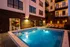 Luxurious apartment complex with a sparkling outdoor swimming pool, stylish poolside loungers, and illuminated ambiance at dusk.