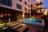 Modern apartment complex at dusk featuring a beautifully lit pool area with inviting lounge chairs and an elegant outdoor fire feature.