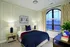 Elegant bedroom featuring a plush bed with navy and burgundy accents, stylish nightstands with lamps, large arched window with serene outdoor view, and tasteful decor creating a tranquil retreat.