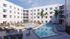 Modern apartment complex featuring a pristine swimming pool, sun loungers, and lush palm trees in a serene courtyard setting.