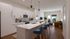 Modern open-plan kitchen and living room with sleek white cabinetry, marble countertops, and comfortable seating, leading to a cozy lounge area with large windows and abundant natural light.