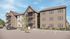 Modern apartment complex exterior showcasing three stories with balconies, surrounded by a serene landscape and spacious parking area.
