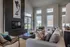 Luxurious living room with a modern fireplace, elegant decor, plush seating, and large windows offering ample natural light and a view of charming apartments outside.
