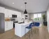 Modern kitchen and living area with sleek white cabinets, elegant island, and stylish blue chairs, complemented by natural light and a touch of greenery.