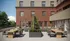 Modern apartment building exterior with stylish outdoor seating area featuring wooden tables and lush greenery, perfect for relaxation and social gatherings.