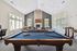 Elegant recreation room featuring a stylish pool table, cozy seating area with a stone fireplace, and abundant natural light from large windows.