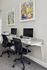 Modern workspace with sleek granite desktop, dual monitors, and ergonomic chairs, accented by colorful wall art.