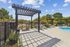 Chic outdoor pool area featuring modern pergola, sun loungers, and a built-in grill, surrounded by lush greenery and vibrant planters.