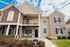 Charming townhouse exterior showcasing a two-story design with a cozy balcony, elegant stonework, and inviting front porches under a bright blue sky.