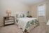 Elegant bedroom with plush carpeting, featuring a stylish bed adorned with paisley-patterned pillows and a cozy quilt, alongside a mirrored nightstand and warm lighting.