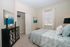 Inviting bedroom with soft pastel decor, featuring a cozy bed, artistic wall paintings, and a charming window view.