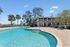 Inviting pool area with crystal clear water, surrounded by lush palm trees and a charming two-story building offering serene views and outdoor relaxation.