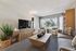Inviting living room with cozy gray sofa, modern wooden furniture, and abundant natural light through large windows.