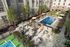 Luxurious apartment courtyard featuring a sparkling swimming pool, shaded lounge areas, lush greenery, and a tennis court, perfect for relaxation and recreation.