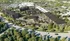 Aerial view of a modern apartment complex surrounded by lush greenery, featuring multiple residential buildings, a central community clubhouse with a pool, and ample parking spaces.
