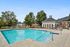 Inviting swimming pool area with lounge chairs, surrounded by lush greenery and charming buildings, under a clear blue sky.