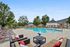 Luxurious outdoor pool area with stylish lounge chairs and elegant clubhouse, surrounded by lush greenery and clear blue skies.