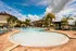 Luxurious outdoor pool area with palm trees, sun loungers, and cabanas under a vibrant blue sky.