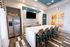 Modern kitchen with a sleek island, stainless steel refrigerator, and chic barstools, featuring trendy artwork and contemporary tile flooring.