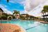 Luxurious apartment complex featuring a stunning pool area with palm trees, ample seating, and bright sunny skies.
