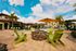 Inviting outdoor space with vibrant green chairs surrounding a stylish fire pit, set amidst a luxurious apartment complex with lush palm trees and a sparkling pool under a bright blue sky.