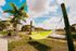 Tropical paradise with vibrant yellow hammocks under swaying palm trees, set against charming apartment buildings and a serene waterfront view.