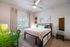 Inviting bedroom with modern decor, featuring a cozy bed with plush pillows, tall window with sheer curtains, and stylish wall art for a serene ambiance.