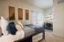 Cozy bedroom with stylish decor, soft cushions, natural light from large window, and a neat workspace featuring wall shelves.