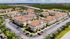Charming aerial view of a Mediterranean-style apartment community with terracotta roofs and lush landscaping, adjacent to a tranquil pond and surrounded by scenic greenery.