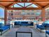 Charming covered patio with vibrant blue cushioned seating, overlooking a pristine swimming pool and elegant brick apartment facade.