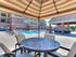 Inviting outdoor area with modern patio seating under a striped canopy, overlooking a pristine swimming pool and sunlit apartment complex.