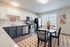 Modern kitchen and dining area featuring sleek appliances, elegant cabinetry, and a cozy dining table set for four, illuminated by natural light from large windows.