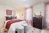 Charming bedroom with modern decor featuring a cozy bed with colorful cushions, stylish artwork, pink curtains, and a sleek dresser.
