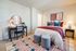 Cozy bedroom with stylish decor, featuring a plush bed, modern desk, and vibrant artwork, illuminated by warm lighting.