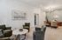 Elegant apartment lounge area with plush green armchairs, a stylish round coffee table, and a sophisticated office desk under a modern chandelier.