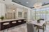 Elegant kitchen and dining area featuring a sleek island with bar stools, modern pendant lighting, and a chic chandelier, complemented by large windows with plantation shutters.