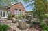 Charming outdoor patio with stylish wicker furniture set against a backdrop of lush greenery and elegant brick architecture.