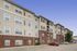 Charming multi-story apartment building with modern exterior and ample parking space, set against a clear blue sky.