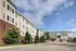 Charming multi-story residential building with attractive brick and siding facade, nestled in a lush green setting under a bright blue sky.