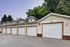 Charming row of garages with classic white doors and elegant gabled roofs, set in a lush, tree-lined community.