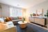 Charming living room featuring a cozy L-shaped sofa, vibrant cushions, and natural light from a large window, complemented by stylish decor and lush greenery.