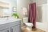 Elegant bathroom with modern fixtures, purple shower curtain, and a lush plant, offering a glimpse into a cozy bedroom.