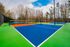 Vibrant outdoor tennis court with colorful blue and green surfaces, surrounded by lush trees and bright skies.