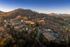 Scenic aerial view of a beautifully landscaped apartment complex nestled among rolling hills and lush forests, highlighted by warm sunset hues.