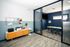 Modern office space with sleek glass-walled meeting room, stylish wooden cabinet, printers, and vibrant wall art.